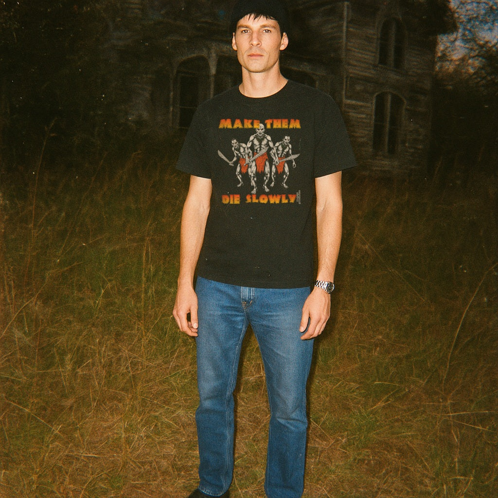 Person wearing a black t-shirt with graphic design and text, standing in front of an old building at night.