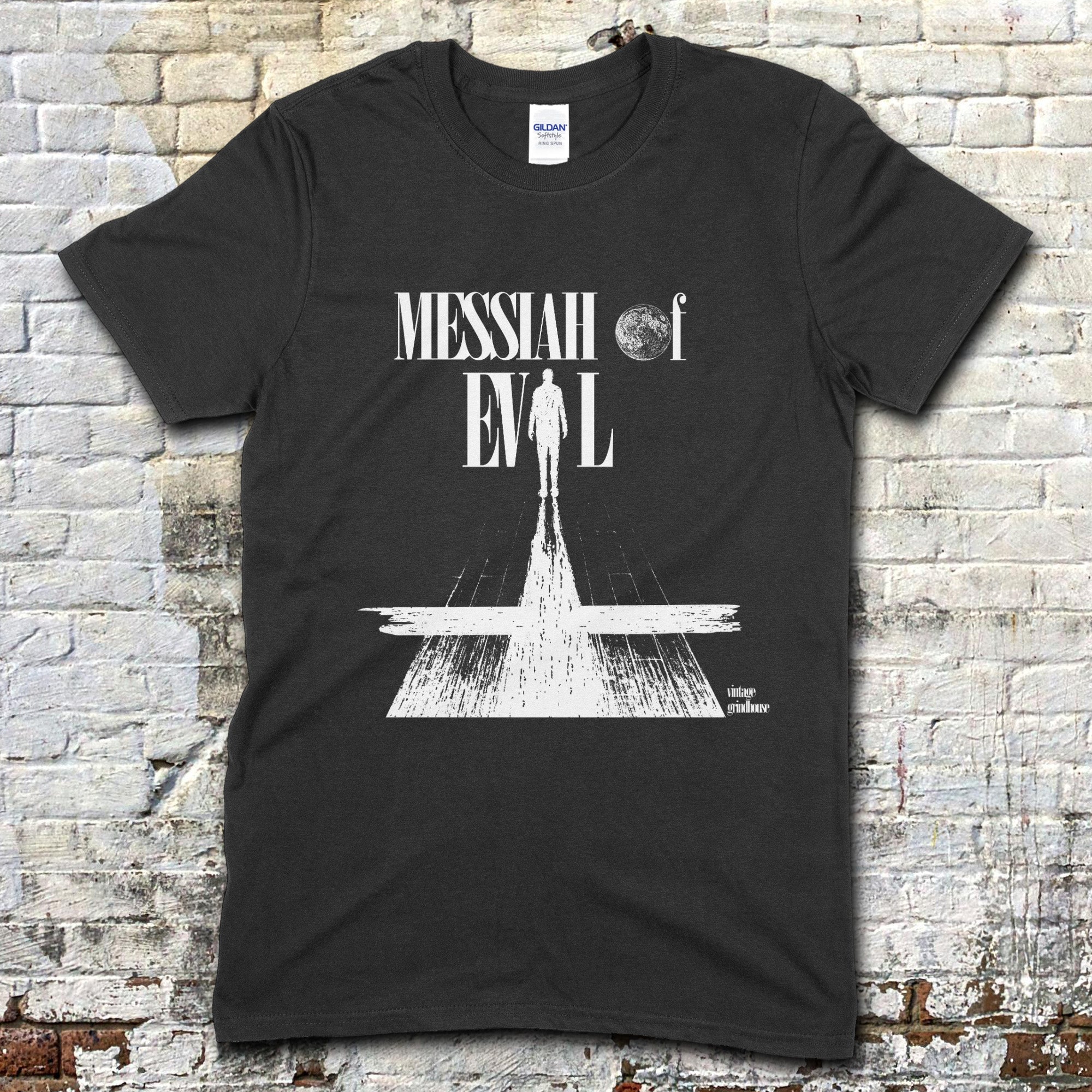 Black t-shirt with white graphic design featuring a silhouette and text, against a brick wall background.