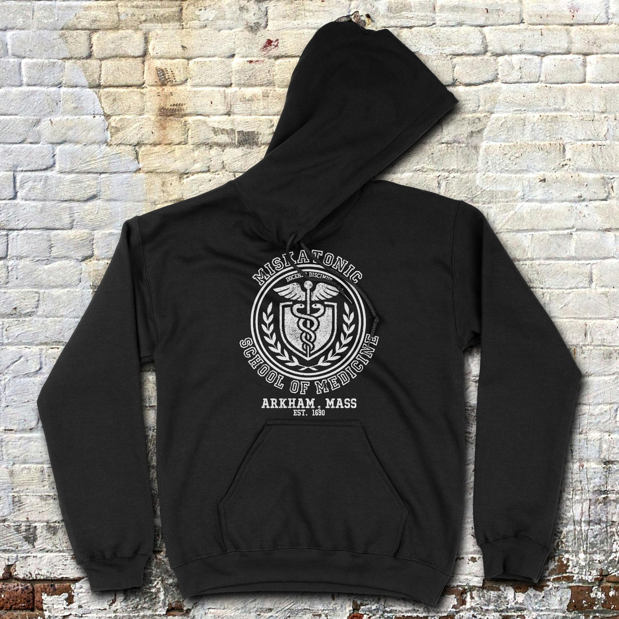 Black hoodie with a graphic design on the back against a brick wall.