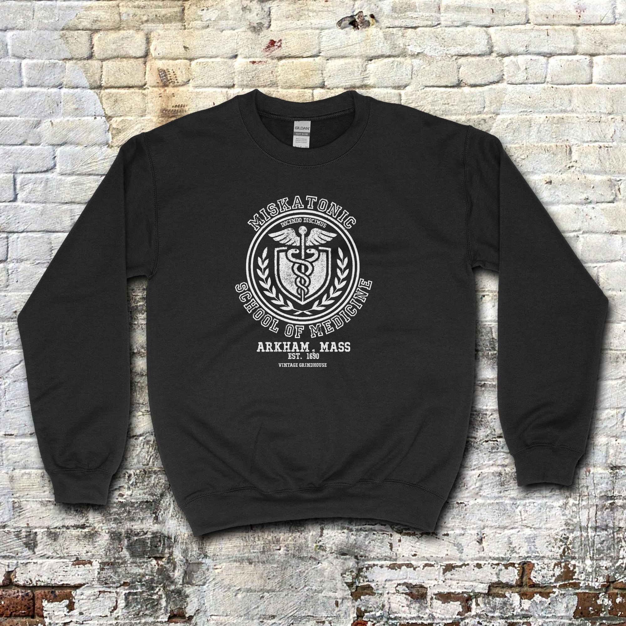 Black Miskatonic School of Medicine sweatshirt featuring a classic medical emblem with caduceus and laurel wreath design.