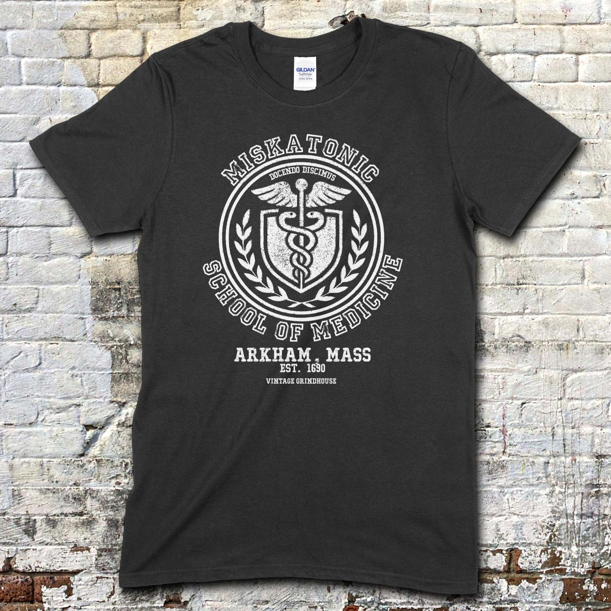 Black t-shirt featuring a vintage medical crest graphic with Miskatonic School of Medicine and Arkham, Mass text on front