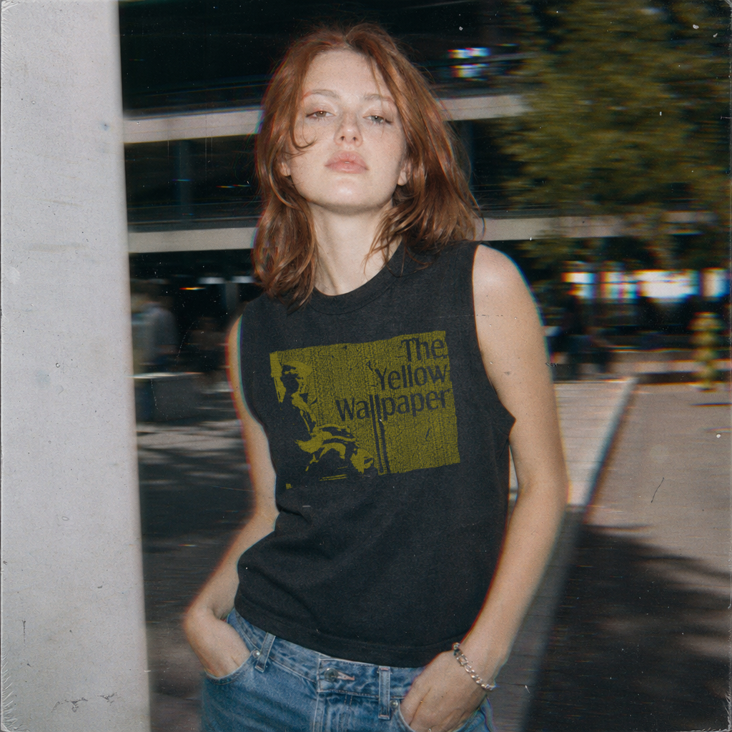 Model wearing The Yellow Wallpaper muscle tank with vintage-style yellow graphic on black fabric outdoors