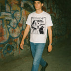 Person wearing a white t-shirt with graphic design in front of a graffiti-covered wall