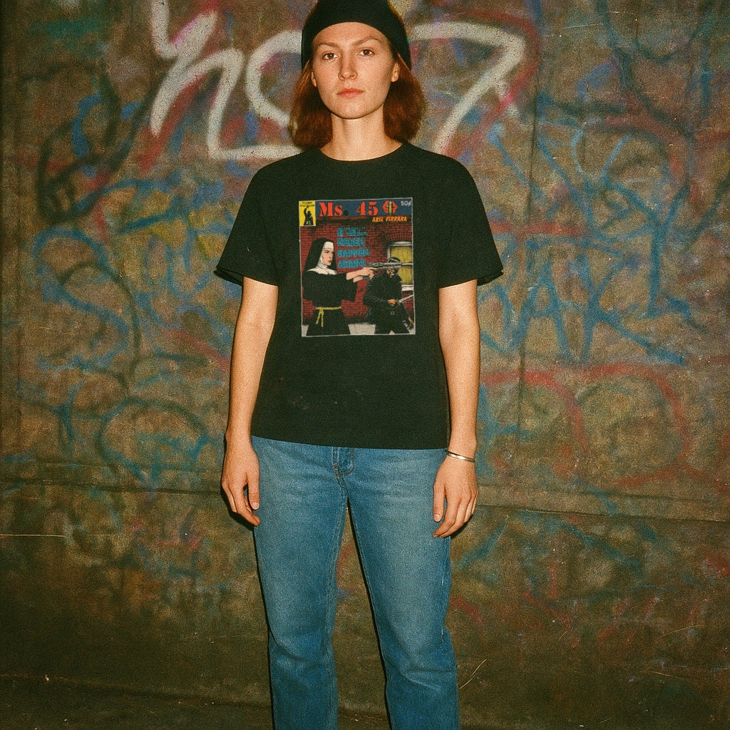 Person wearing a black t-shirt with a graphic design in front of a graffiti-covered wall.