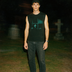 Model wearing Nosferatu: A Symphony of Horror muscle tank with eerie vampire silhouette design in vintage grindhouse style at night.