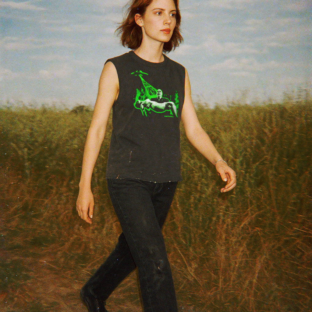 Woman walking outdoors wearing Plan 9 from Outer Space muscle tank with vivid green alien and spaceship graphic on dark fabric