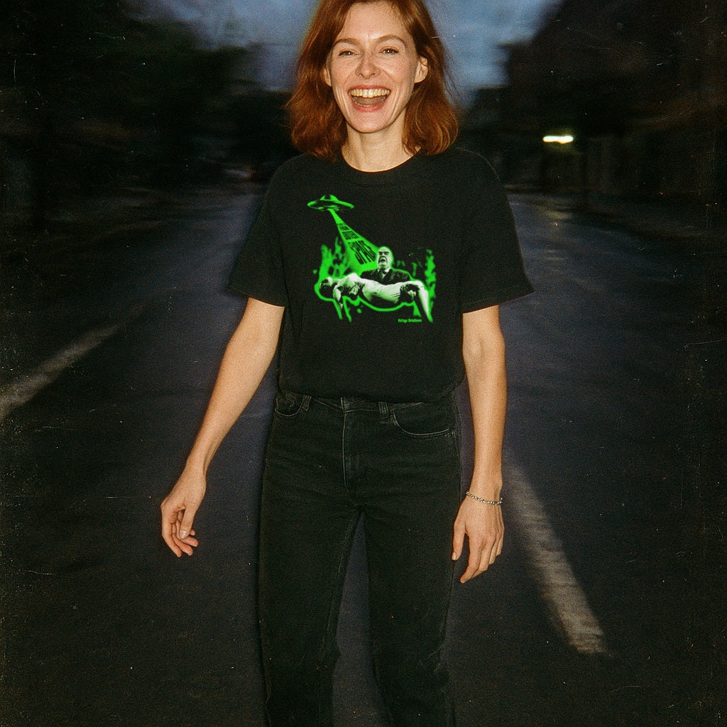 Person wearing a black t-shirt with a green graphic design on a dark road.