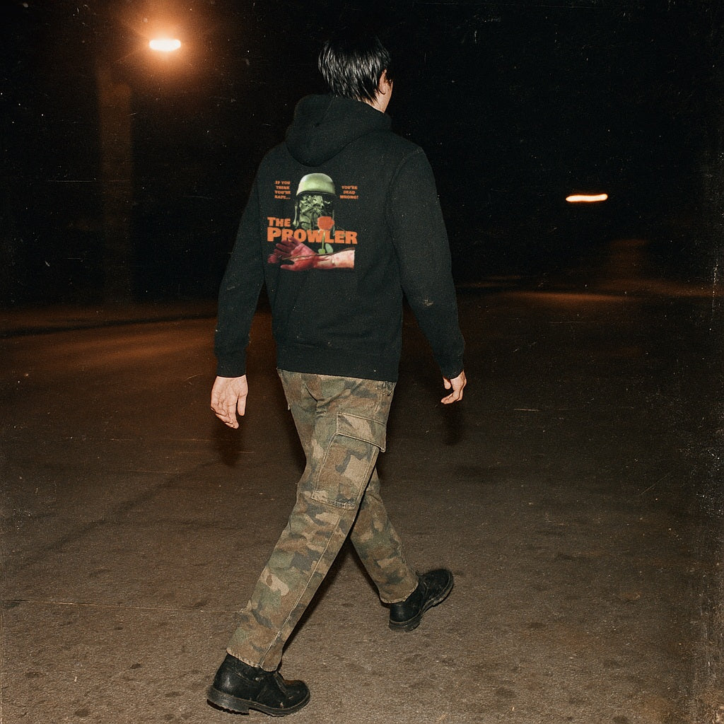 The Prowler hoodie (rear print) with vintage horror scene and bold orange text worn by person walking at night