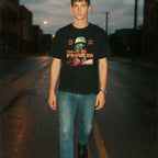 Person wearing a black t-shirt with graphic design on a dark street.