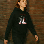 Person wearing Tenebrae hoodie with striking horror-inspired graphic and red text walking by brick wall at dusk