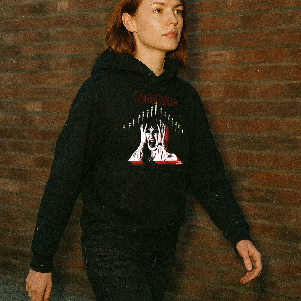 Person wearing Tenebrae hoodie with striking horror-inspired graphic and red text walking by brick wall at dusk