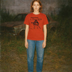 Person wearing a red t-shirt with graphic design in an outdoor setting with a car in the background