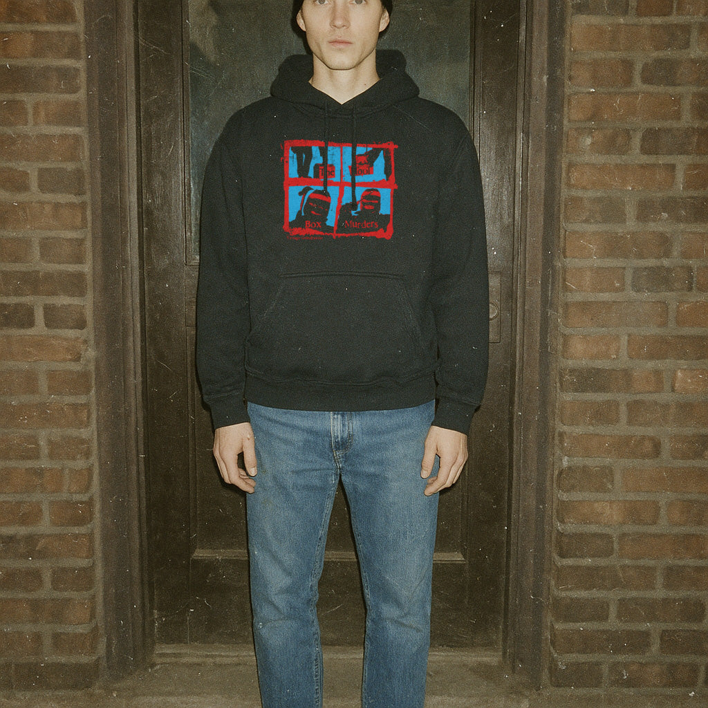 Person wearing a black hoodie with a red and blue graphic design in front of a brick wall.