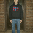 Person wearing a black hoodie with a red and blue graphic design in front of a brick wall.