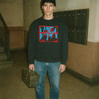 The Toolbox Murders sweatshirt with red-framed horror images and text on black fabric worn by man holding vintage toolbox