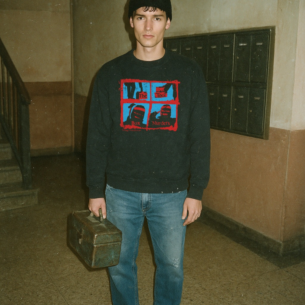 The Toolbox Murders sweatshirt with red-framed horror images and text on black fabric worn by man holding vintage toolbox