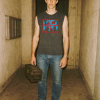 The Toolbox Murders muscle tank worn by model holding vintage toolbox with red and blue graphic on faded black fabric