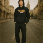 Person wearing a black hoodie with 'TORSO' printed on it in an urban setting