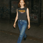 Torso muscle tank with distressed yellow lettering worn by model walking in dimly lit urban setting