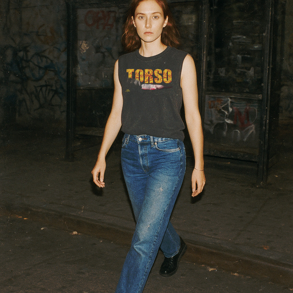 Torso muscle tank with distressed yellow lettering worn by model walking in dimly lit urban setting