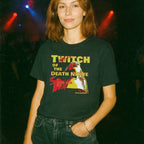 Woman wearing black Twitch of the Death Nerve t-shirt featuring bold yellow and red graphic design at a concert venue