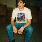 Man sitting on a stool wearing a graphic t-shirt with a zombie design in an indoor setting.